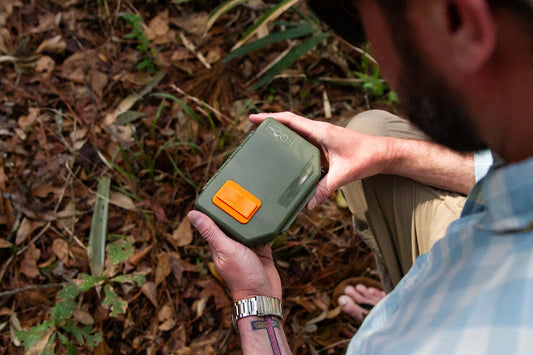 A fly fisherman holding an olive Atollas 1GO Fly Box outside in the forest