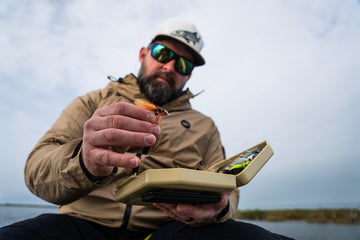 A fly angler holding an Atollas 2GO Fly Box and placing fly into the box with cloudy sky in background