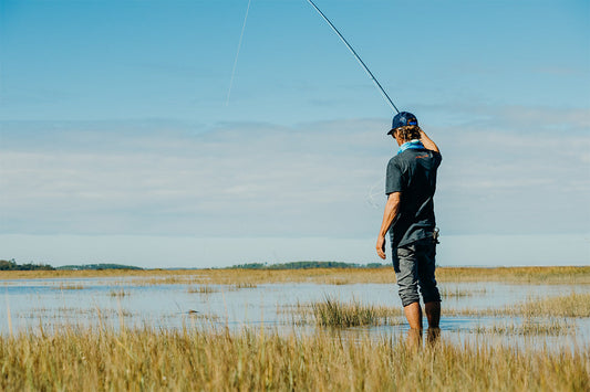 fly fisherman wading a flooded marsh flat catching a redfish