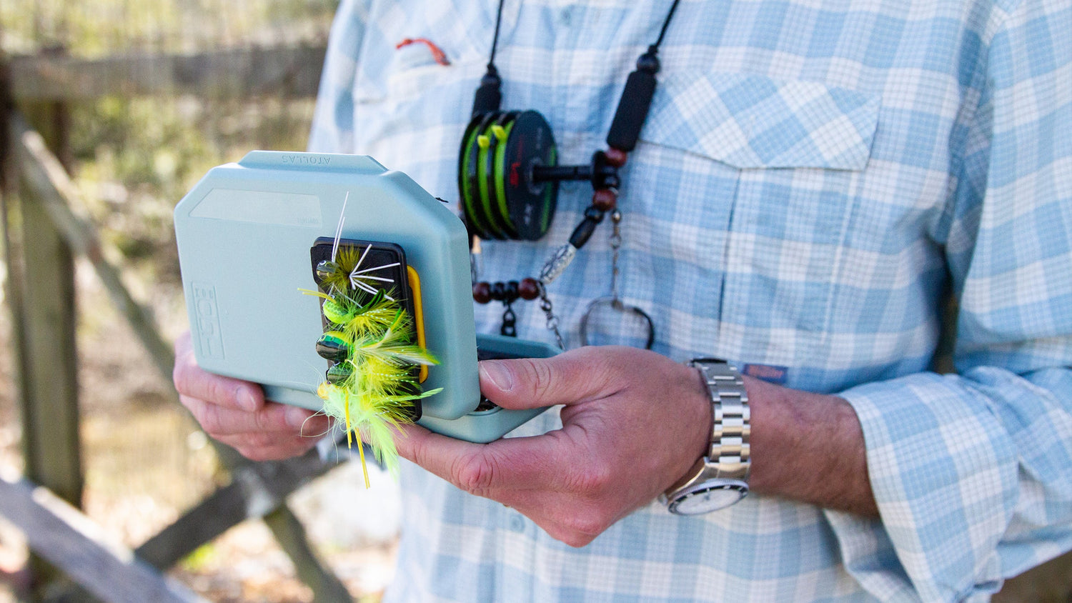 Fly angler holding an open Flats Green 1GO Fly Box with Fly Caddy clippable fly patch attached to with assorted flies outside