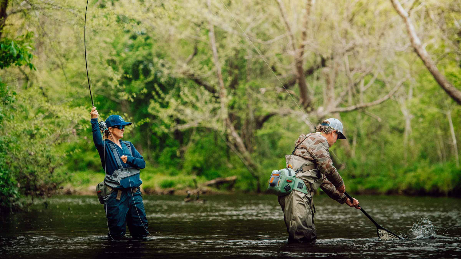 Fly angler outdoors catching a trout wading in a stream in the outdoors