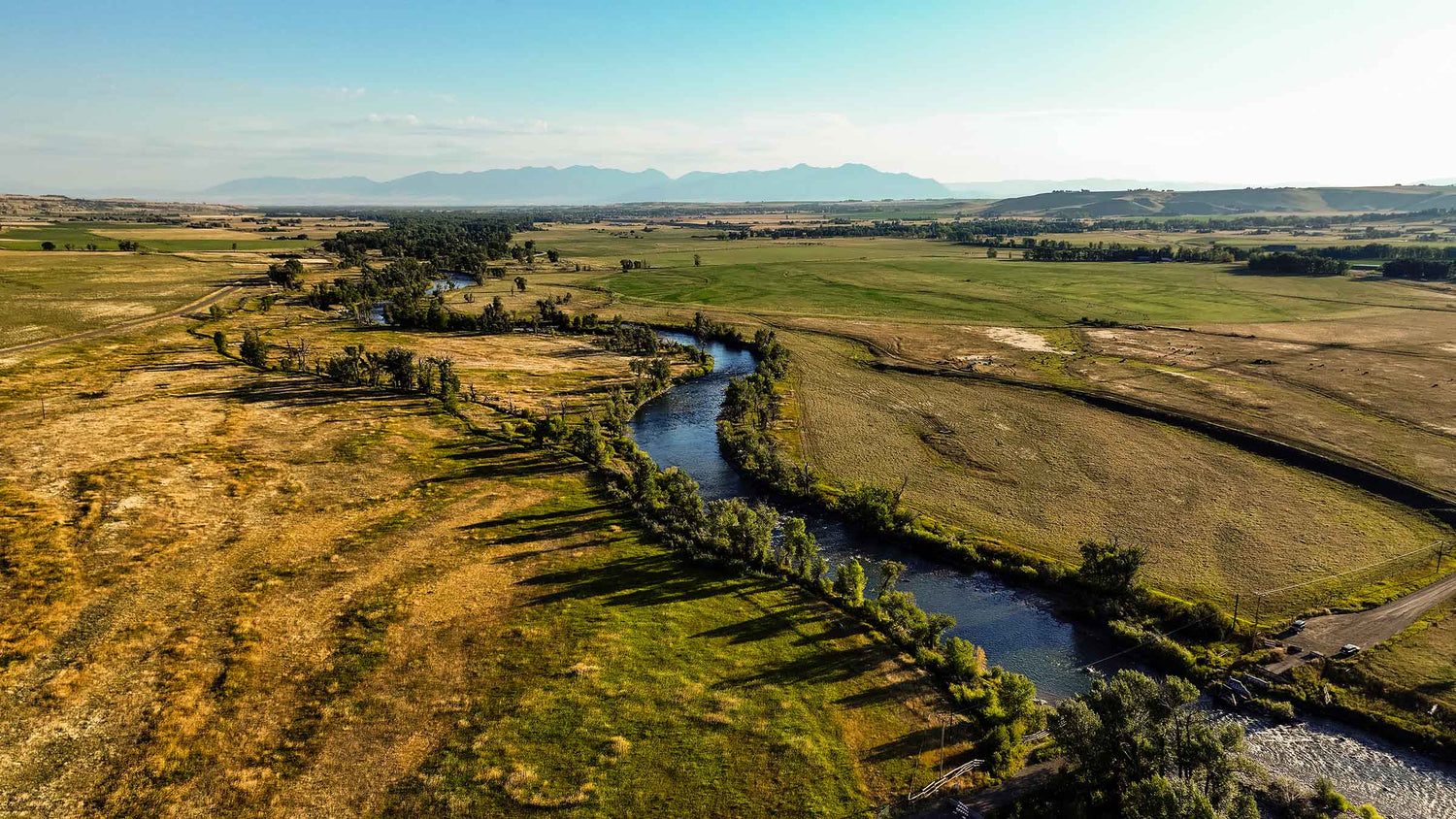 Aerial view of a winding river cutting through fields with mountains in distance