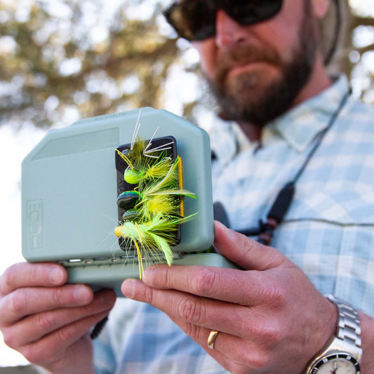 Fly angler holding a green Atollas 1GO Fly Box with a Fly Caddy clippable fly patch attached to the outside of it