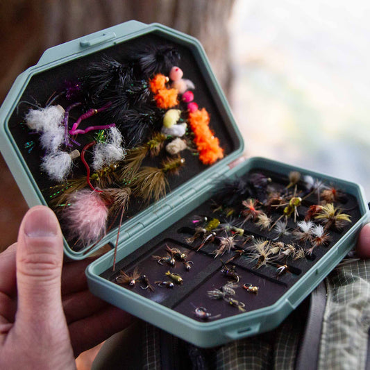 Hand holding an open green Atollas 1GO Fly Box with assorted flies outside