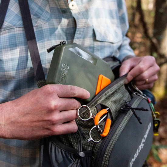 Fly angler holding an olive Atollas 1GO Fly Box and placing it into a sling pack outdoors