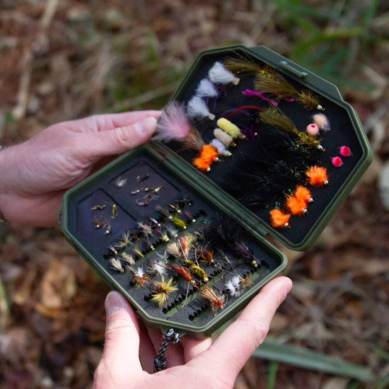 Hand holding an olive Atollas 1GO Fly Box opened with assorted flies outdoors