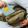 A person holding a green 2GO Fly Box and packing it into a Patagonia waist pack