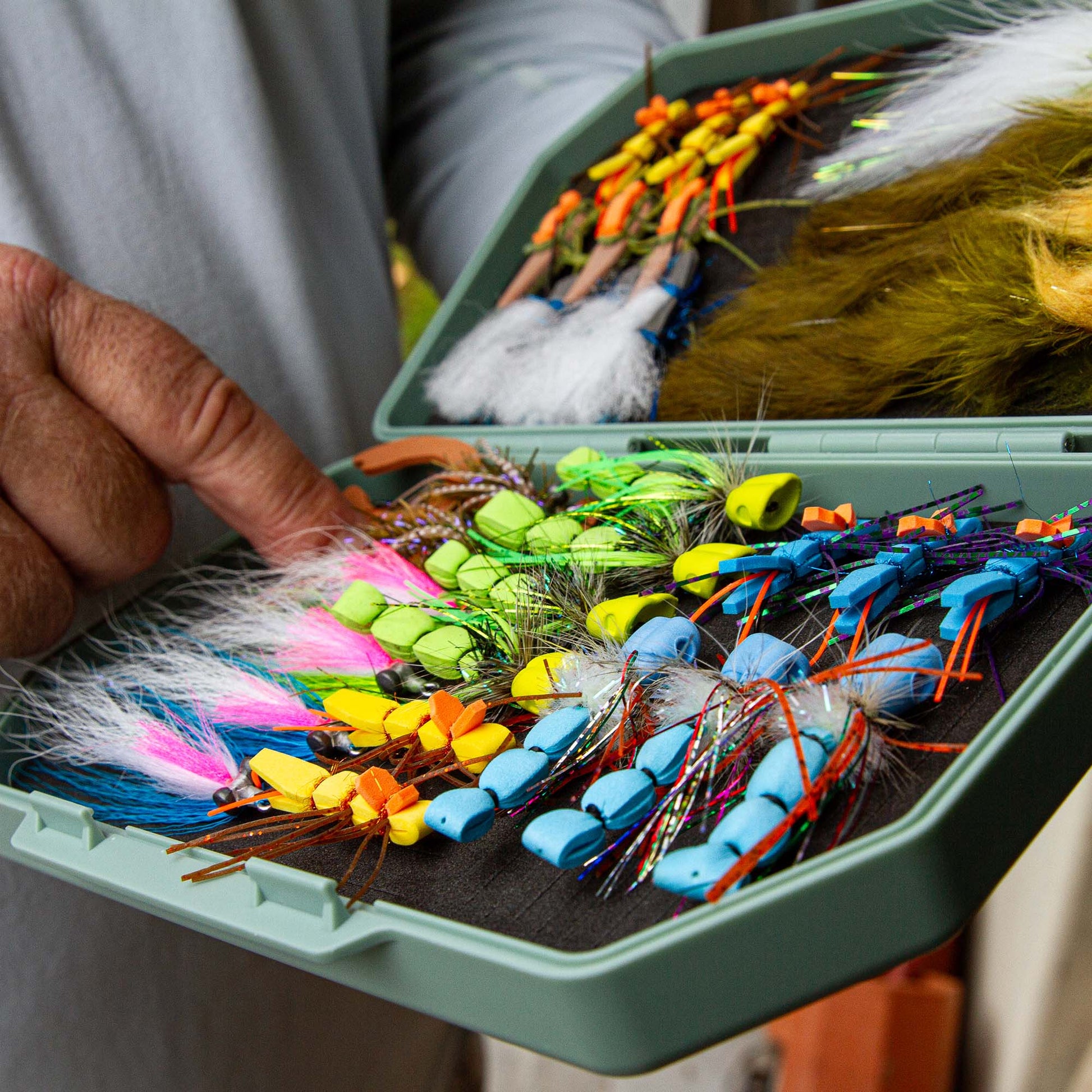 An Atollas 2GO Fly Box opened with assorted colorful flies held by a fly angler