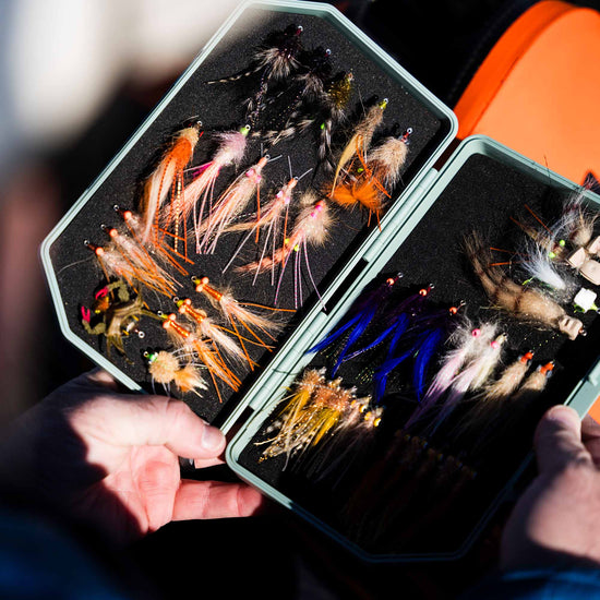 An Atollas 2GO Fly Box opened in hand displaying various saltwater flies with a blurred background