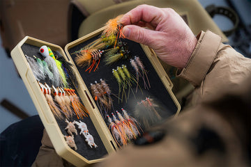 Hand holding an Atollas 2GO Fly Box with various fly fishing flies inside.