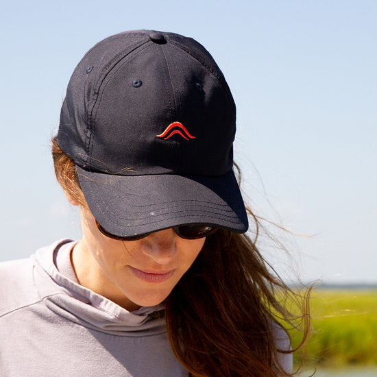 Person wearing a navy blue cap with a red Atollas logo outdoors