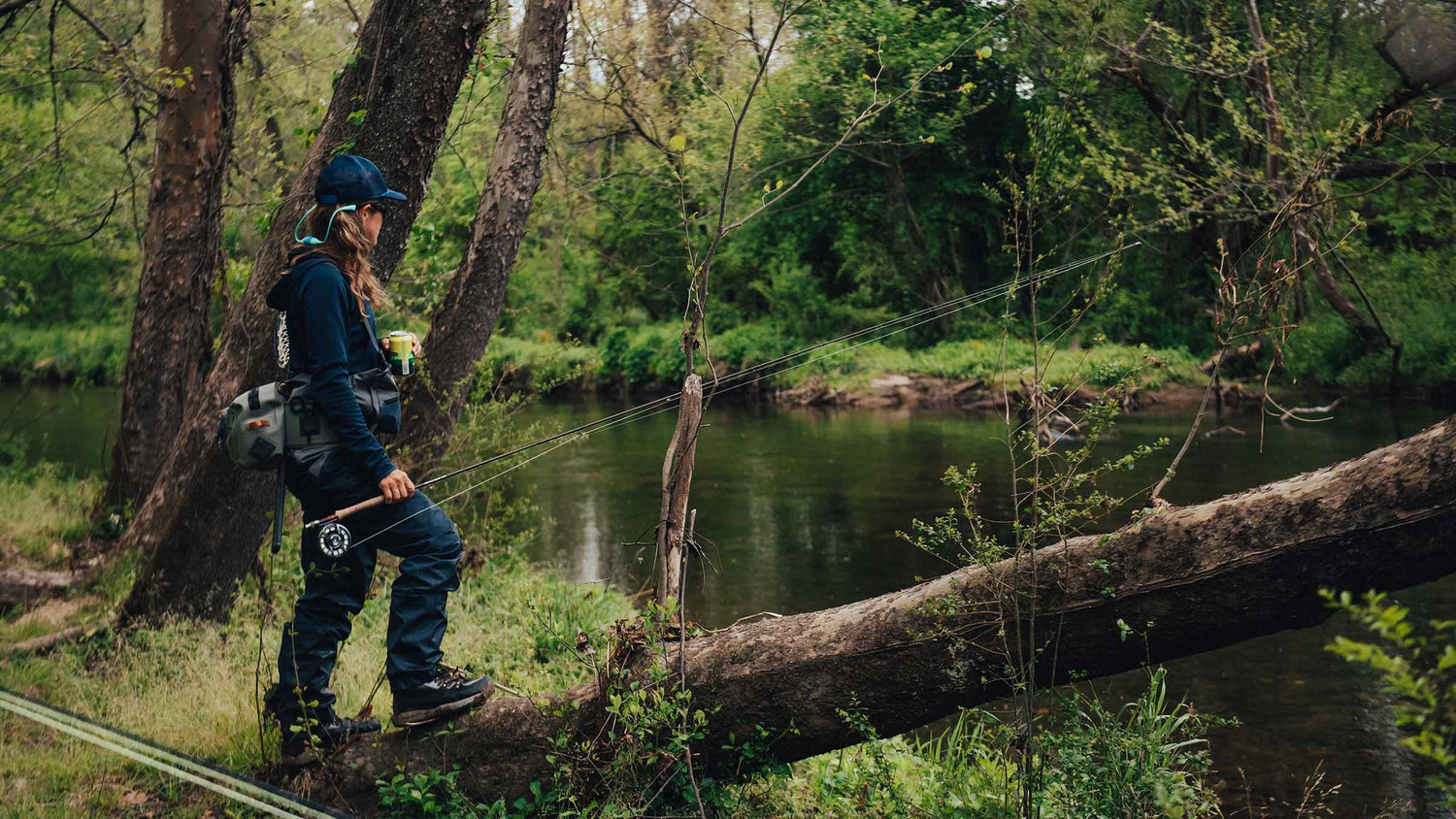 Person fly fishing by a stream in a forested area