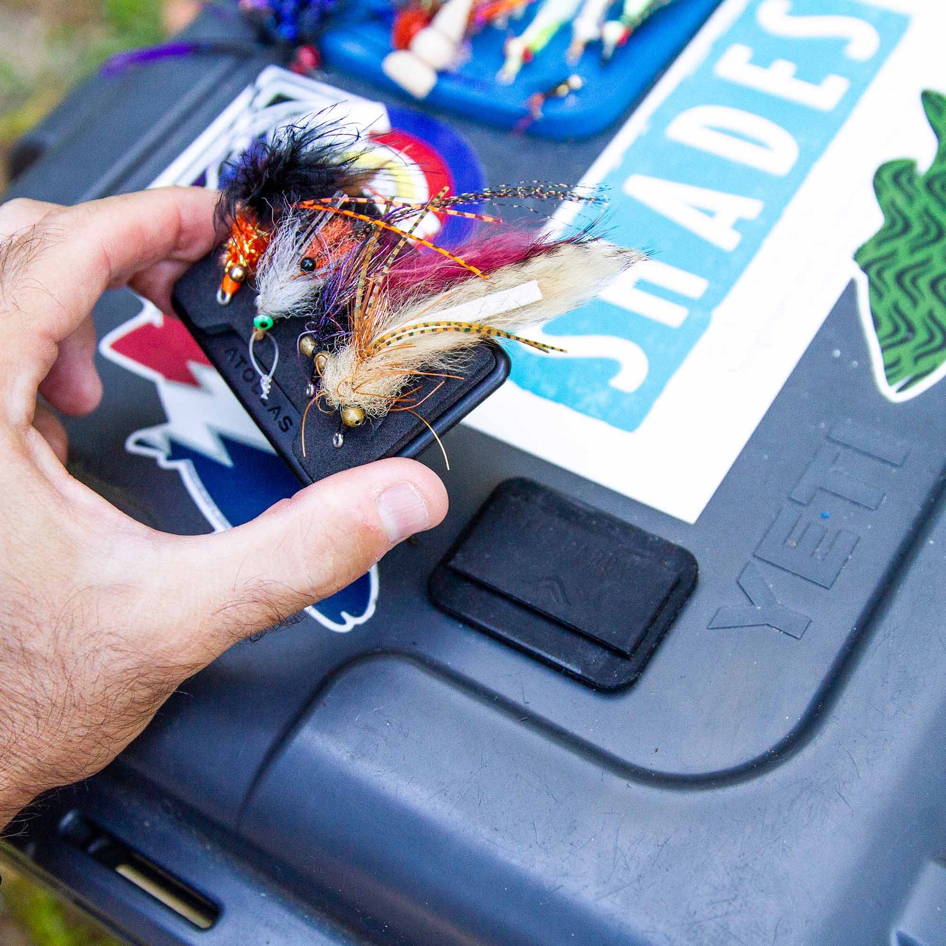 Hand holding an Atollas Fly Caddy fly patch and clipping it to a docking station attached to a YETI loadout box