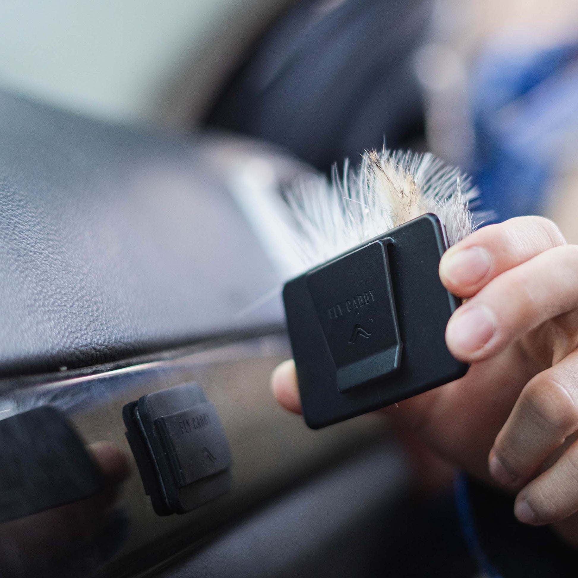 A person holding an Atollas Fly Caddy fly patch showing the clip on the backside next to a docking station it clips to which is adhered to the dash of a vehicle