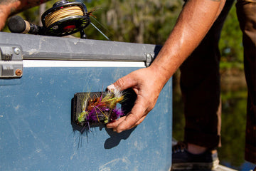 Person reaching for a Fly Caddy XL clippable fly patch that is docked on a cooler via the included docking station