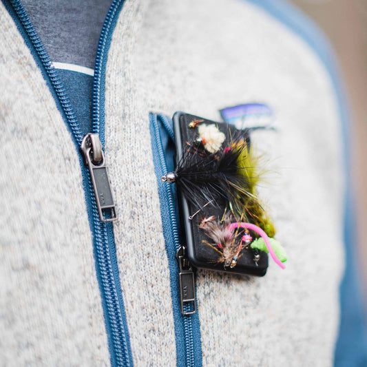 An Atollas Fly Caddy fly patch clipped to the chest pocket of a fleece with an assortment of flies attached to it