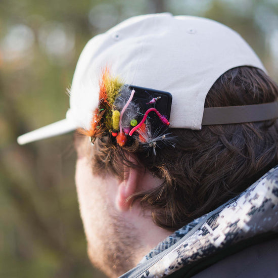 A fly angler with an Atollas Fly Caddy fly patch clipped to the back of his hat displaying assorted flies