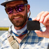 Man holding an Atollas Fly Caddy Velcro adapter outdoors with a clear sky background