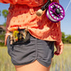Fly angler holding a fly rod with a colorful fly in a natural setting and an Atollas Fly Caddy XL fly patch clipped to their pocket with flies attached to it