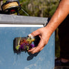 A hand reaching for an Atollas Fly Caddy XL fly patch which is clipped into a docking station attached to a blue cooler with a fly rod on top of it