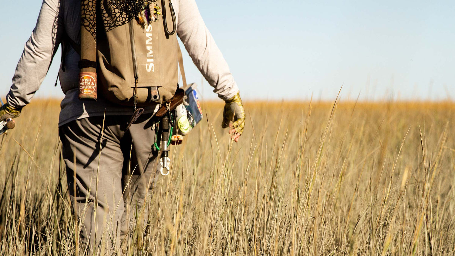 Fly angler wading through marsh grass with fly fishing gear