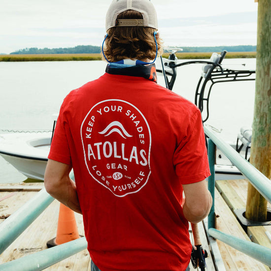Fly angler wearing a red shirt with 'Atollas Gear' branding on a dock heading out to go fish
