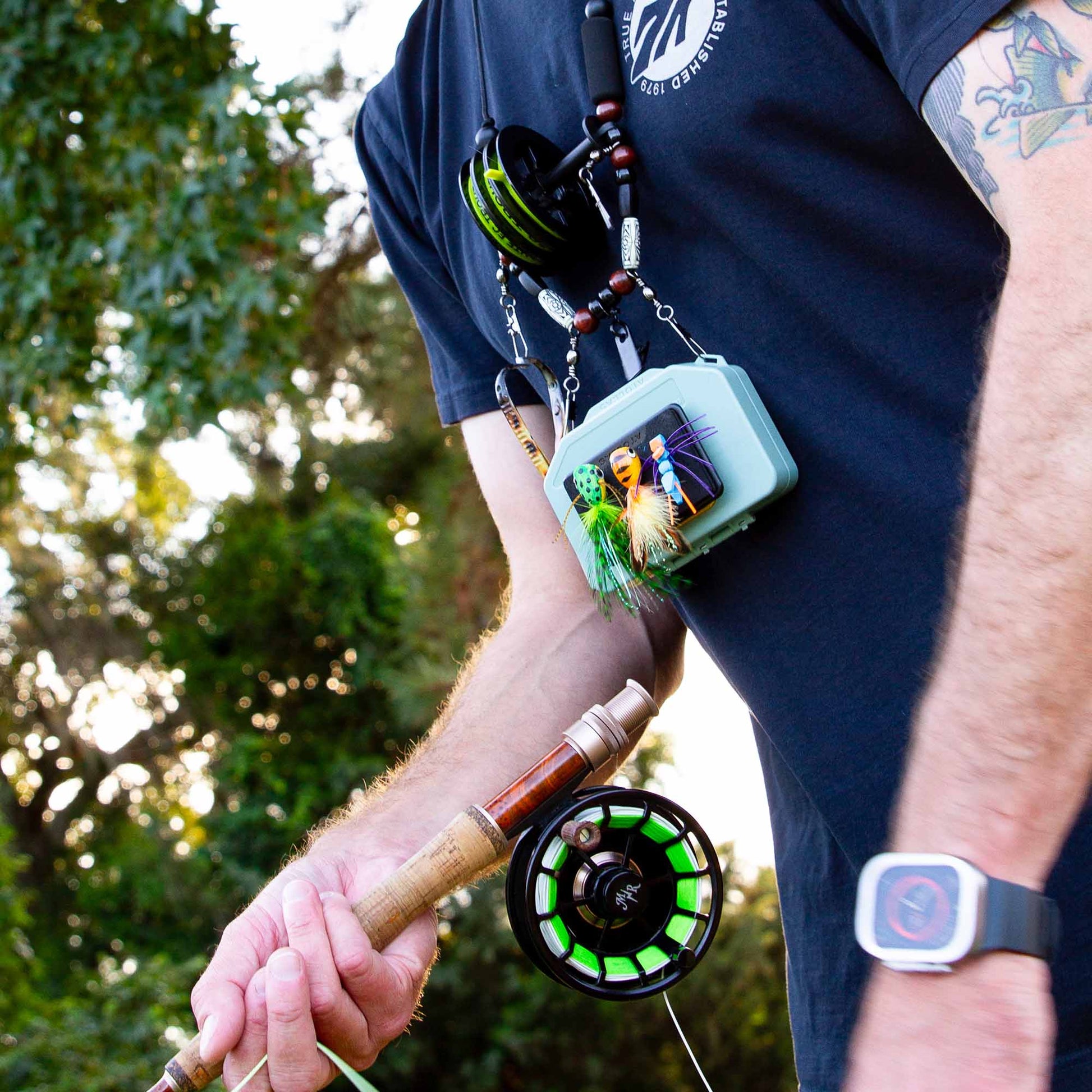 Green Atollas Micro Fly Box clipped to a lanyard with Fly Caddy clippable fly patch attached to the box with flies attached to it, hanging from fly fisherman's neck