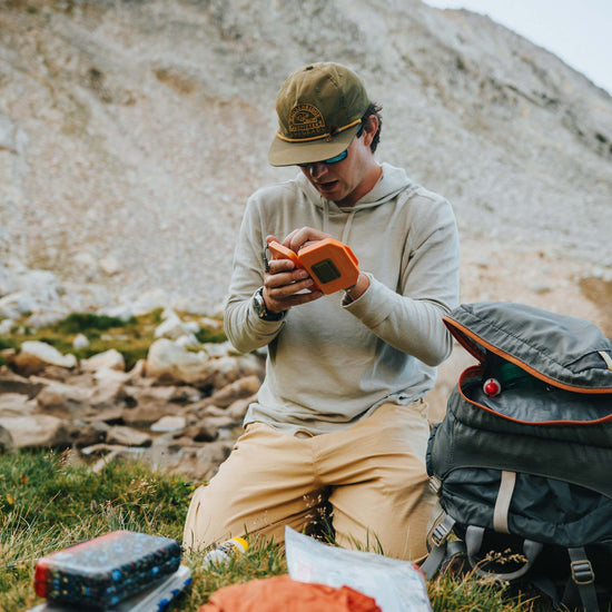Fly angler in outdoor setting using an Atollas Micro Fly Box with mountains in the background
