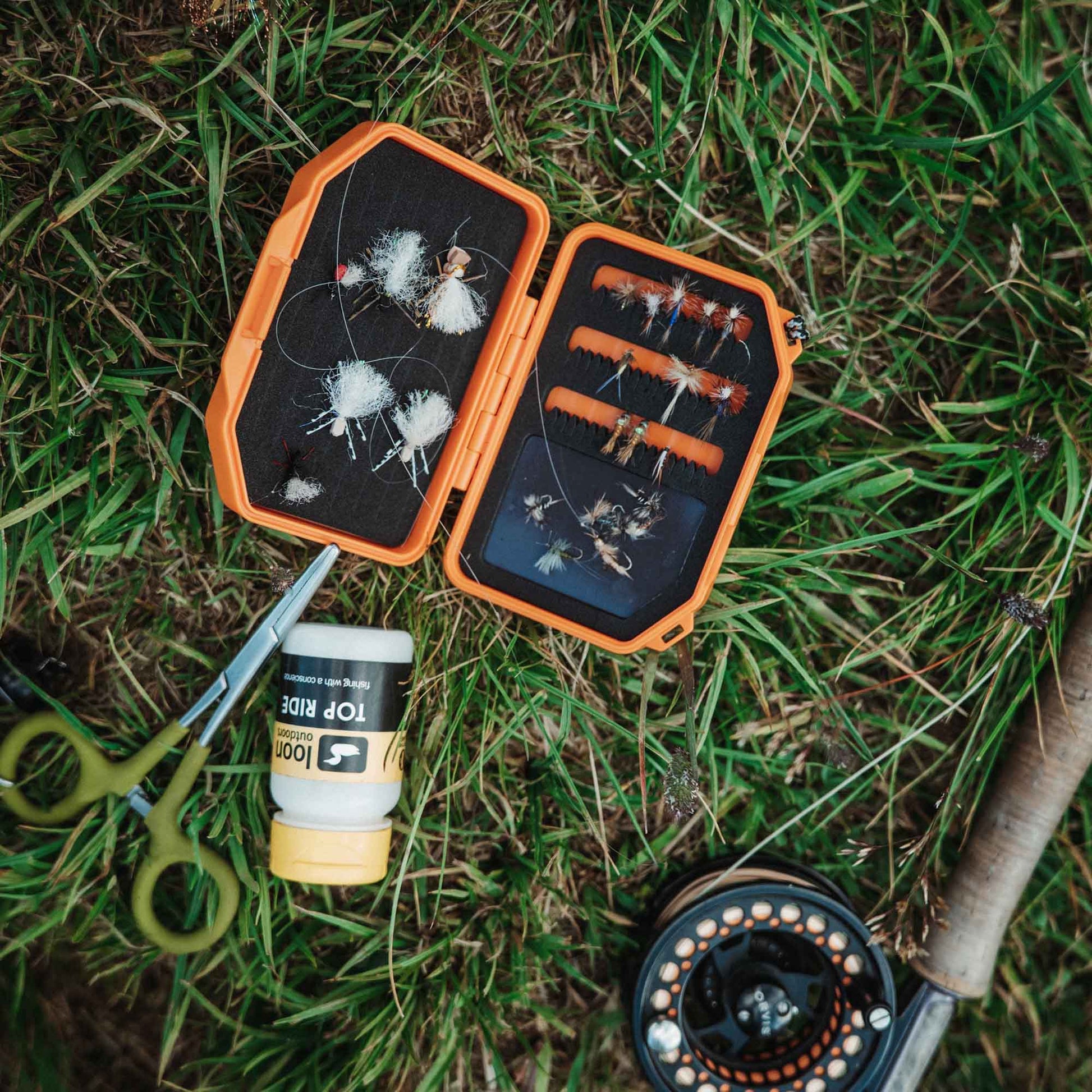 Open Atollas Micro Fly Box fly box with flies, a container, and scissors on grass