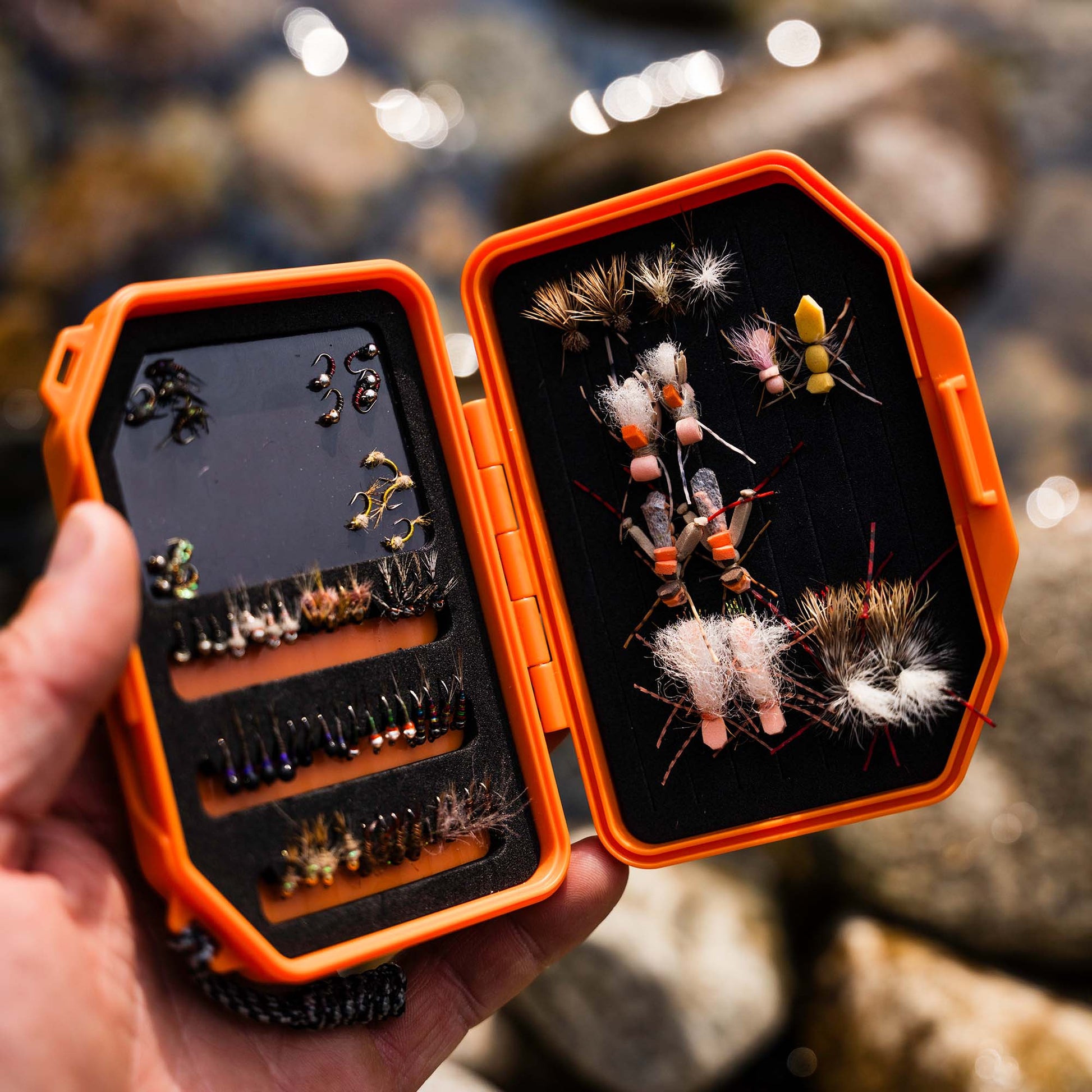 Open Atollas Micro Fly Box displaying various fly fishing flies against a blurred natural background